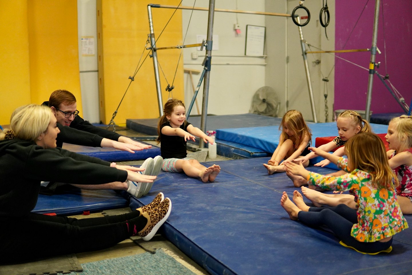 Niños y adultos estirándose sobre colchonetas azules en un estudio de gimnasia.