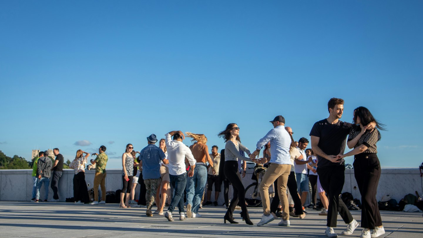 Gente bailando junta en una plaza pavimentada al aire libre.