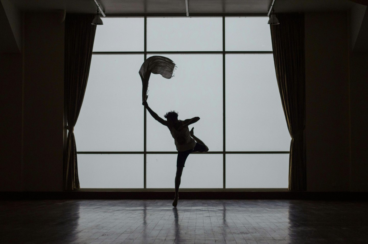 Bailarina en silueta sosteniendo tela a mitad de pose en interiores.